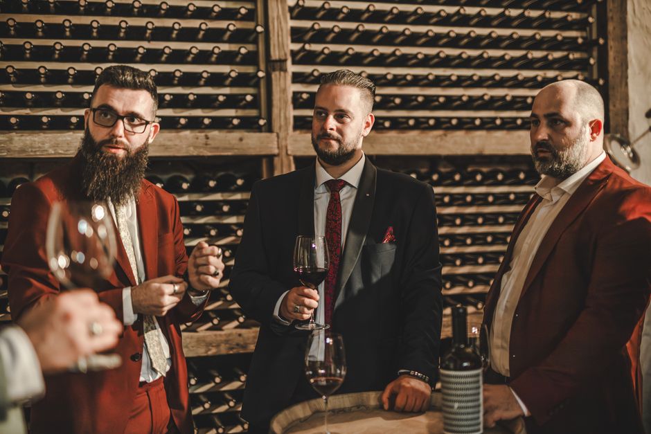 Trojica muškaraca u odijelima uživaju u vinu u sofisticiranom ambijentu vinarije